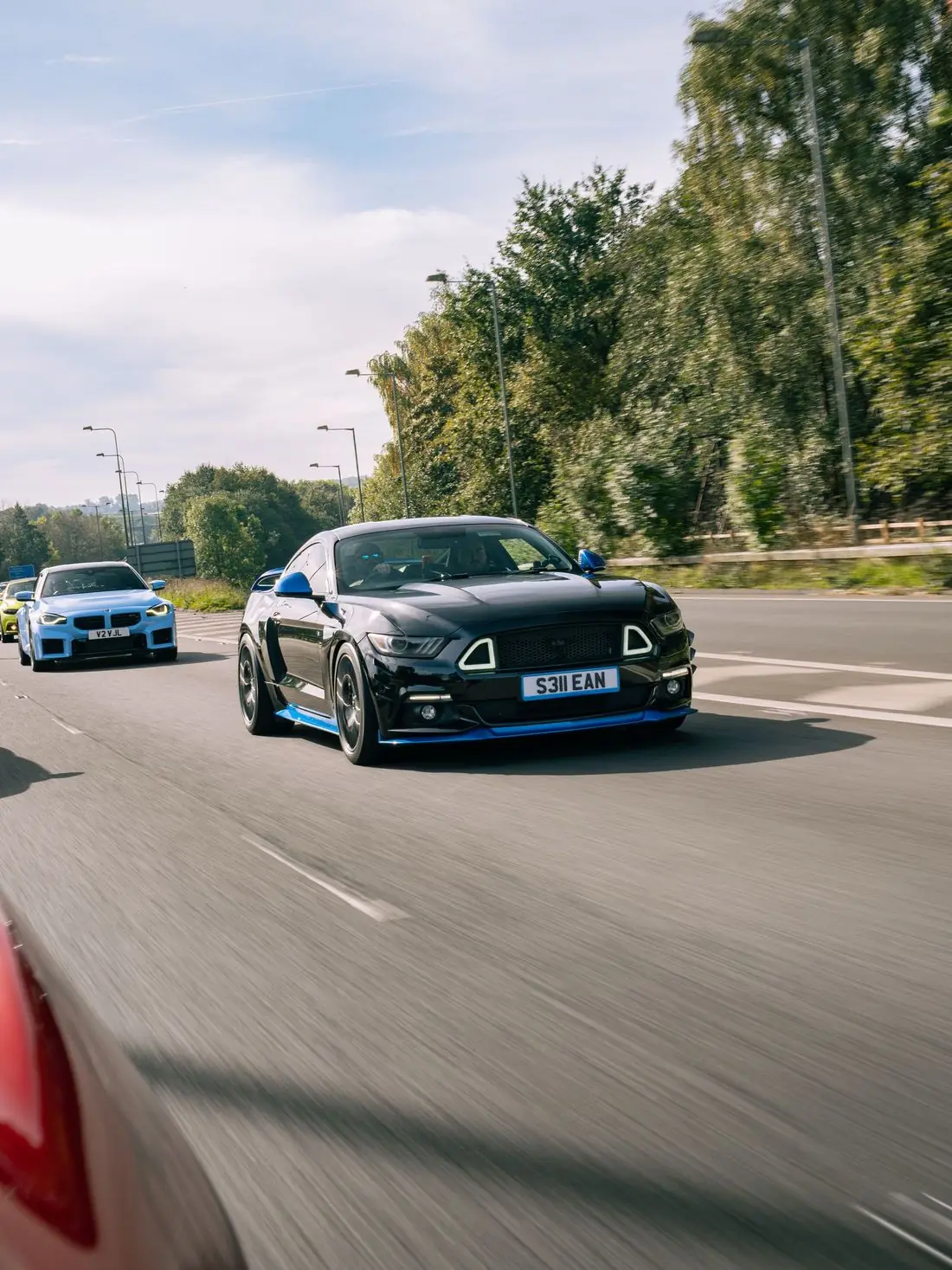 A black Ford Mustang and a blue BMW M2 driving on the road in convoy